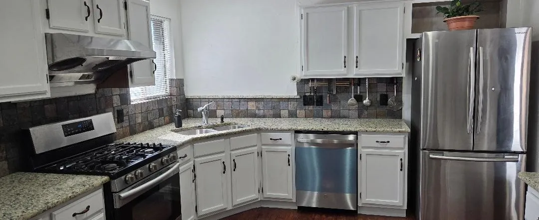 White cabinetry, stainless steel appliances, granite countertops, tile backsplash, and wood-finish flooring