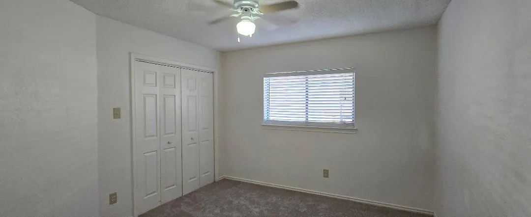 Carpeted room featuring a window with horizontal blinds, a ceiling fan with integrated lighting, and bi-fold closet doors