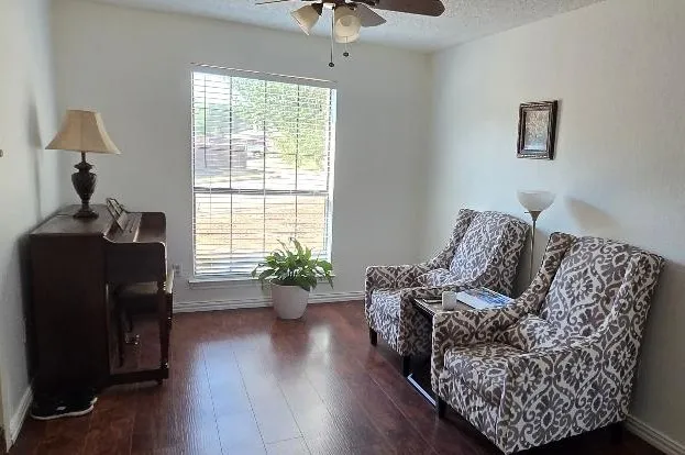 Wood-finish flooring, central window with blinds, ceiling fan, and light-toned wall finishes