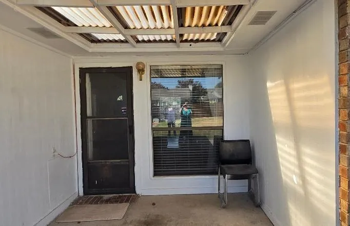 Covered porch entry featuring a corrugated roof, exterior wall sconce, and an expansive window with blinds
