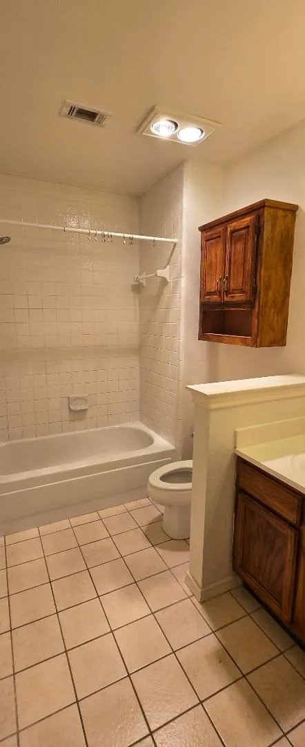 Bathroom featuring a ceramic tile floor, white tub, toilet, wood-finish vanity, and a wall-mounted wood-finish cabinet