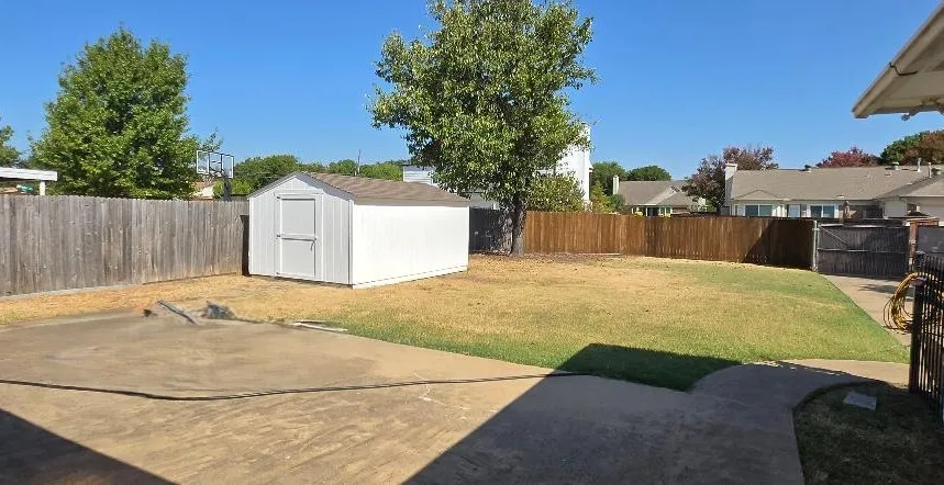 Expansive backyard featuring a concrete patio, a dedicated storage shed, and a wooden privacy fence