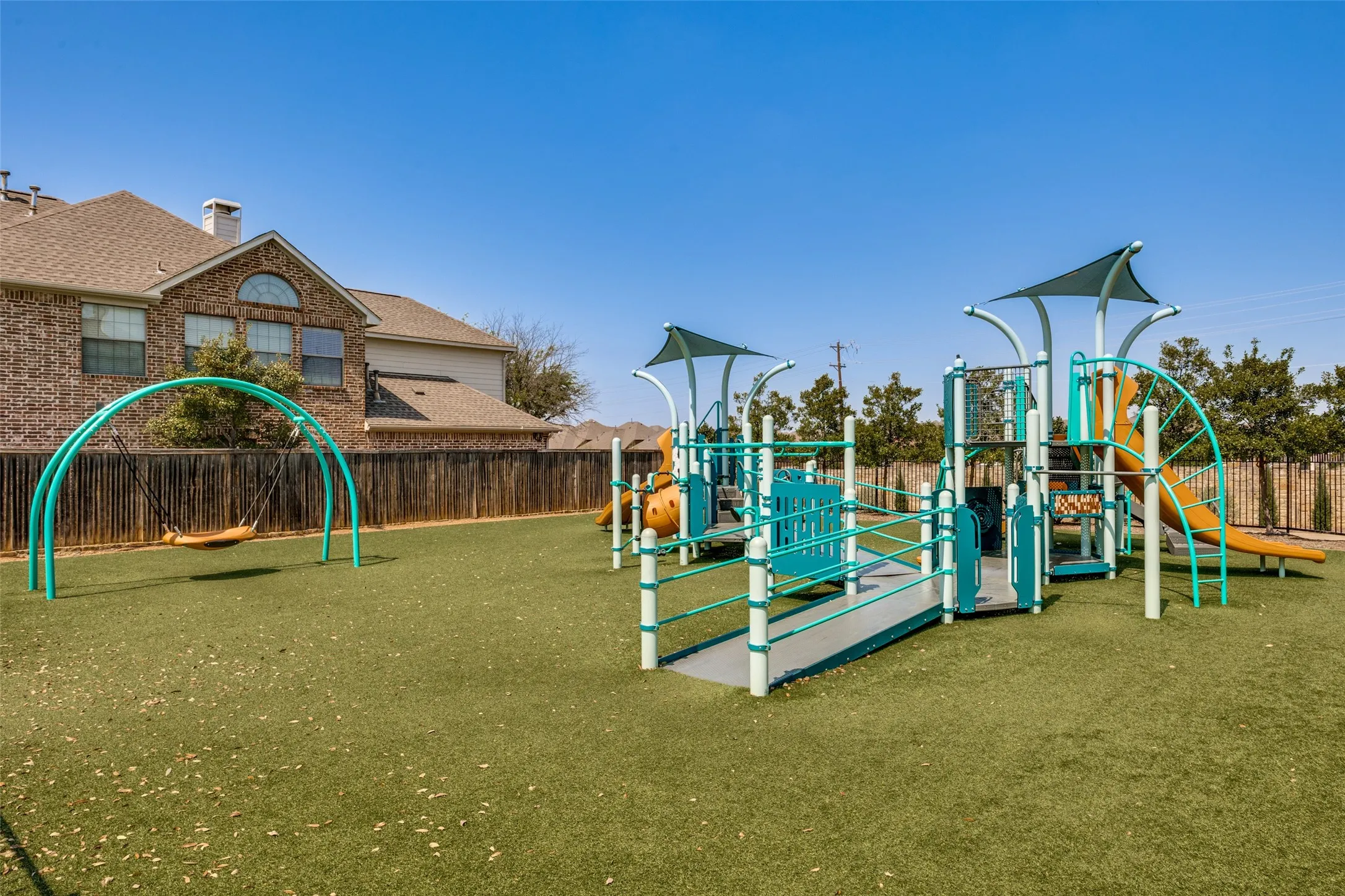 Recreational playground featuring a swing set, multi-level play structure, slides, and shade canopies, all situated on artificial turf