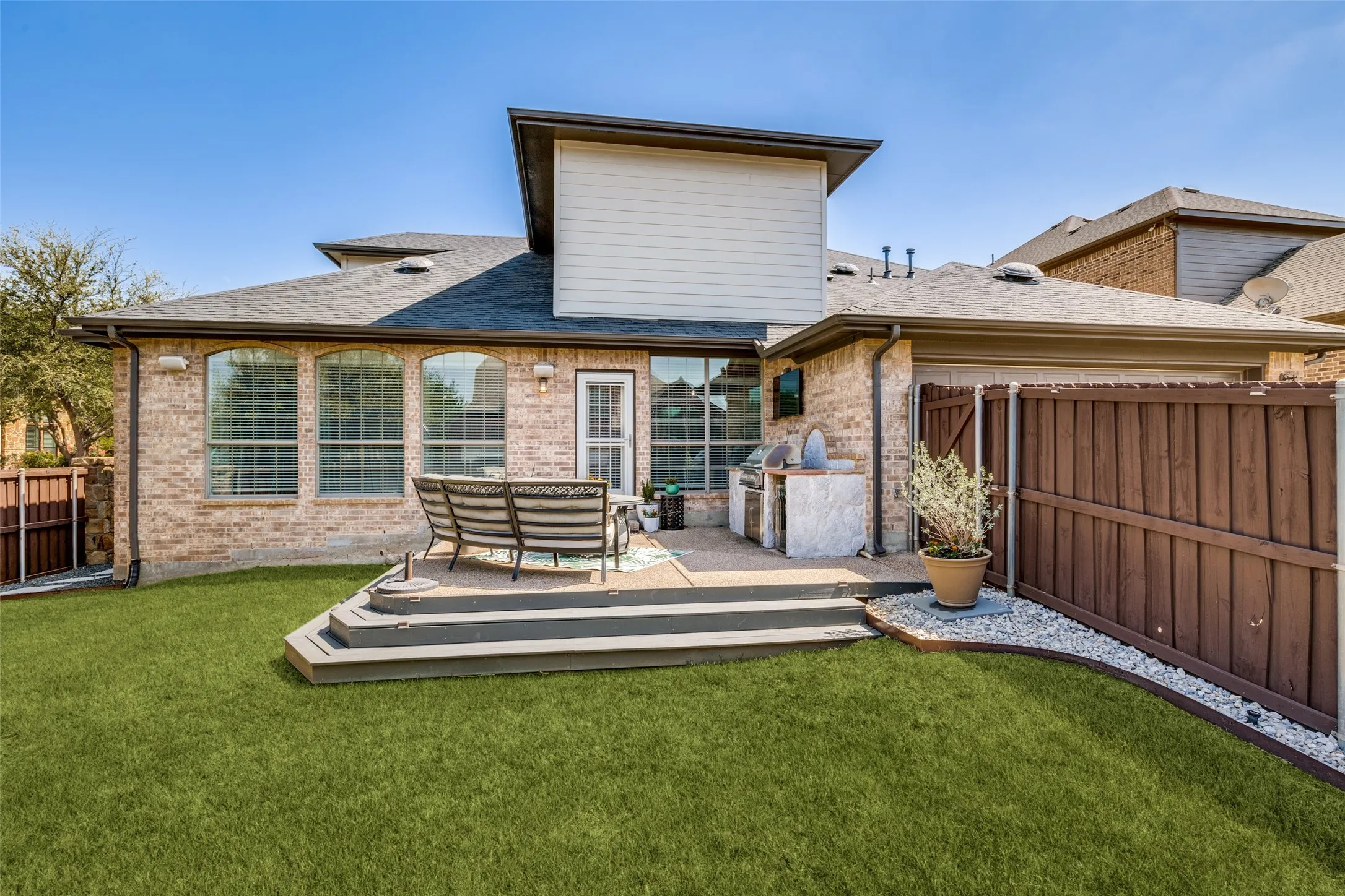 Brick exterior with arched windows, multi-level composite deck, built-in outdoor kitchen, and a privacy fence
