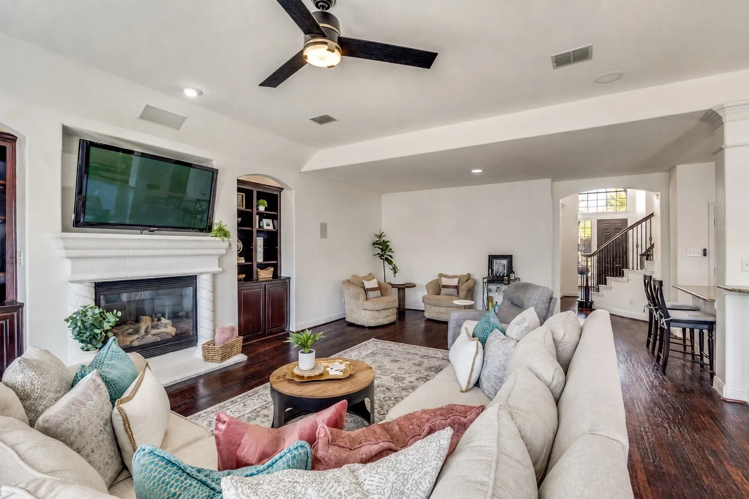 Living area featuring a stone-clad fireplace, built-in shelving, dark wood-finish flooring, and a ceiling fan