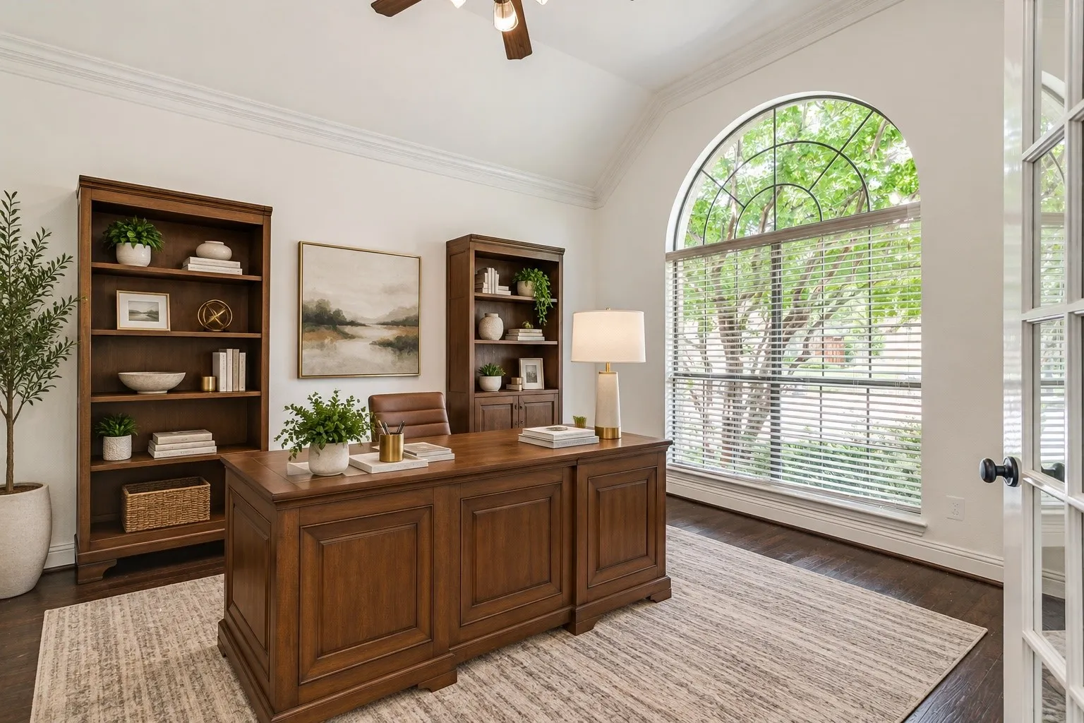 Arched window with exterior tree scenery, vaulted ceiling, crown molding, wood-finish flooring, and French doors
