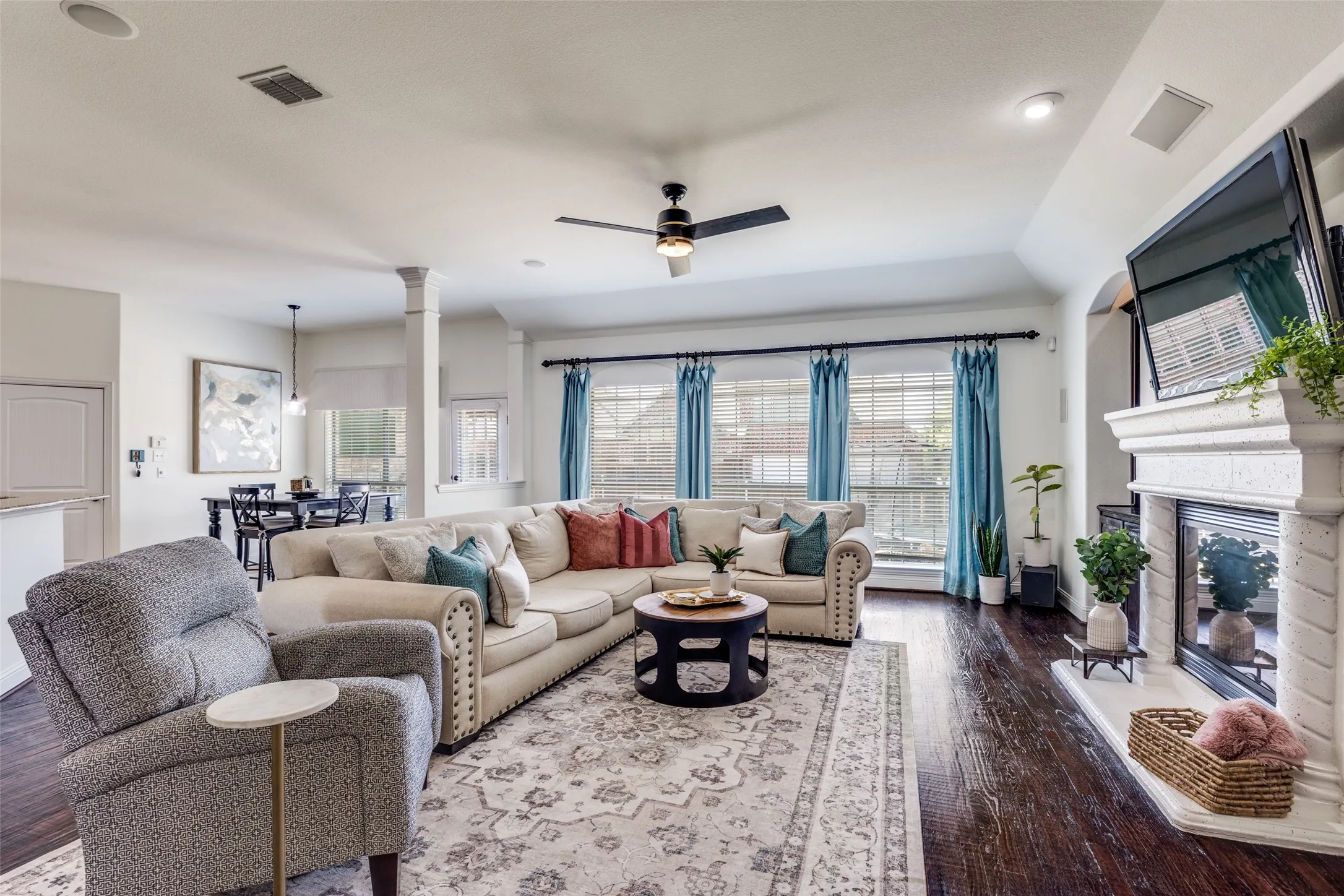 Spacious living area featuring dark wood-finish flooring, a ceiling fan, and multiple windows