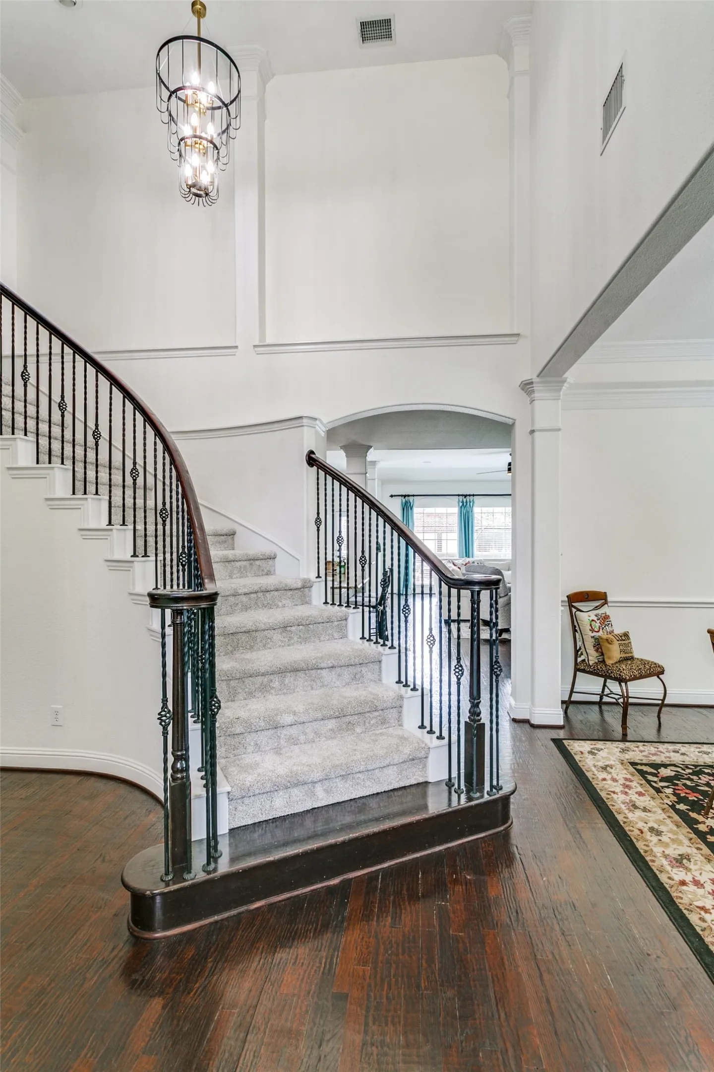 Grand curved staircase with wrought iron balusters, high ceilings, and wood-finish flooring