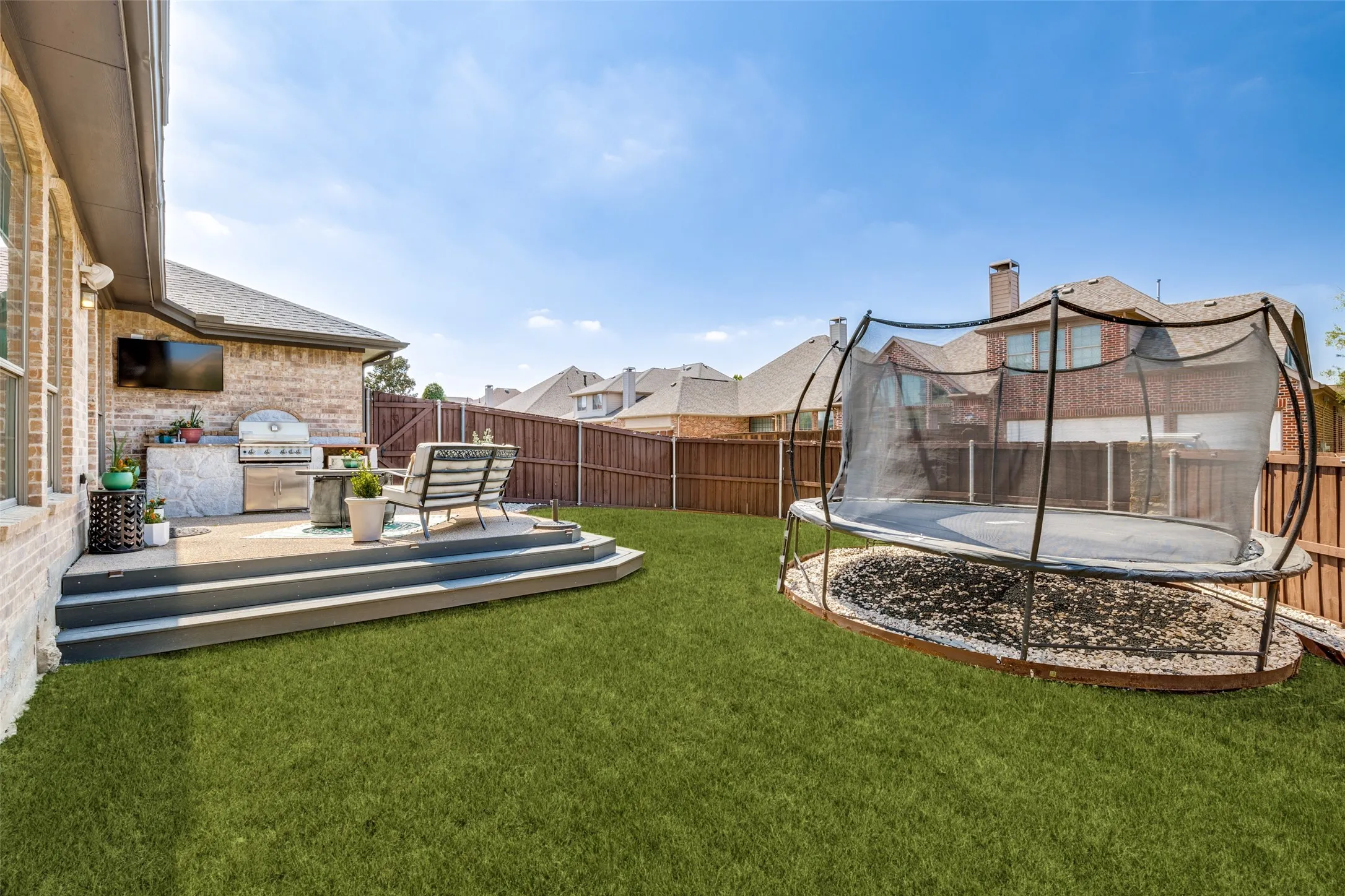 Expansive backyard featuring a built-in outdoor kitchen with a stainless steel grill, a tiered composite deck, and a manicured lawn