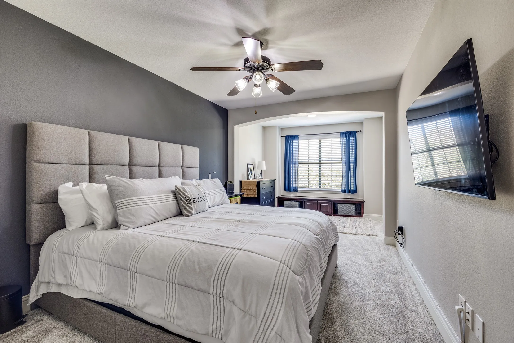 Recessed window alcove with built-in storage bench, ceiling fan with light fixture, and mounted television