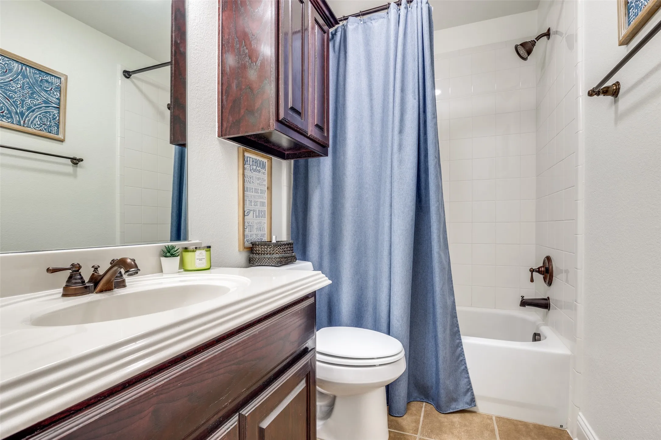 Bathroom featuring a white vanity with an integrated sink, dark wood-finish cabinetry, a full-width mirror, and a tiled shower-tub combination with bronze-finish fixtures