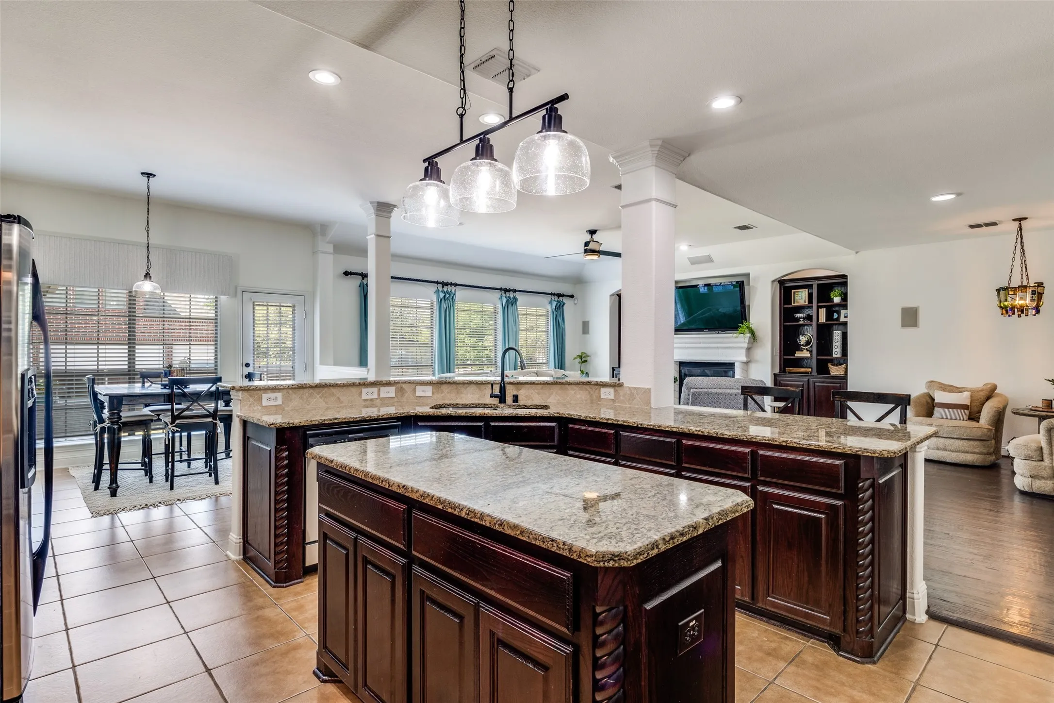 Kitchen featuring an expansive island, granite countertops, dark wood cabinetry, a built-in sink, and tile flooring