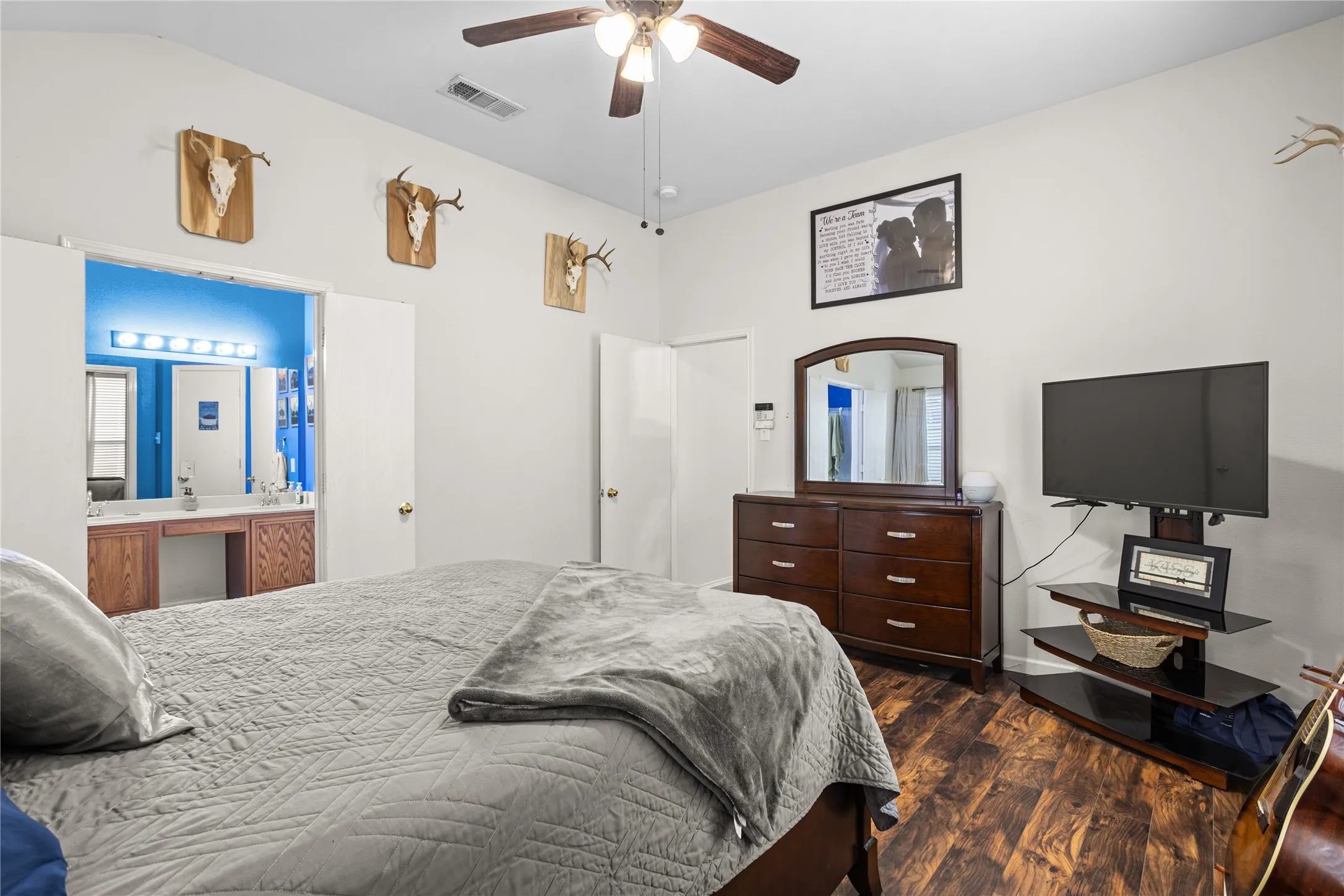 Wood-finish flooring, ceiling fan with light fixture, double doors, and an en-suite bathroom featuring a dual vanity with built-in storage