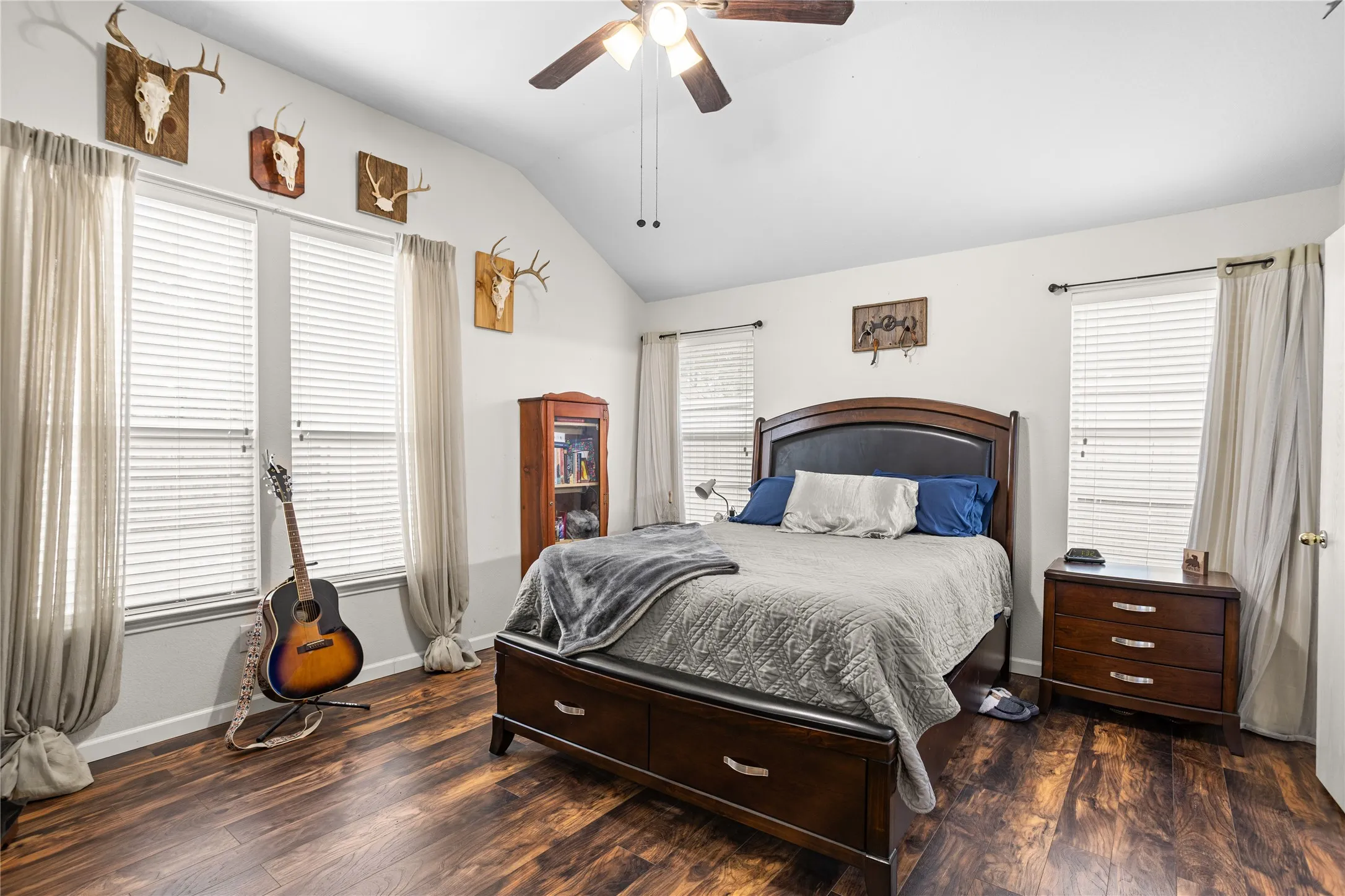 Vaulted ceiling with a ceiling fan, multiple windows with blinds, wood-finish flooring, and crisp white walls