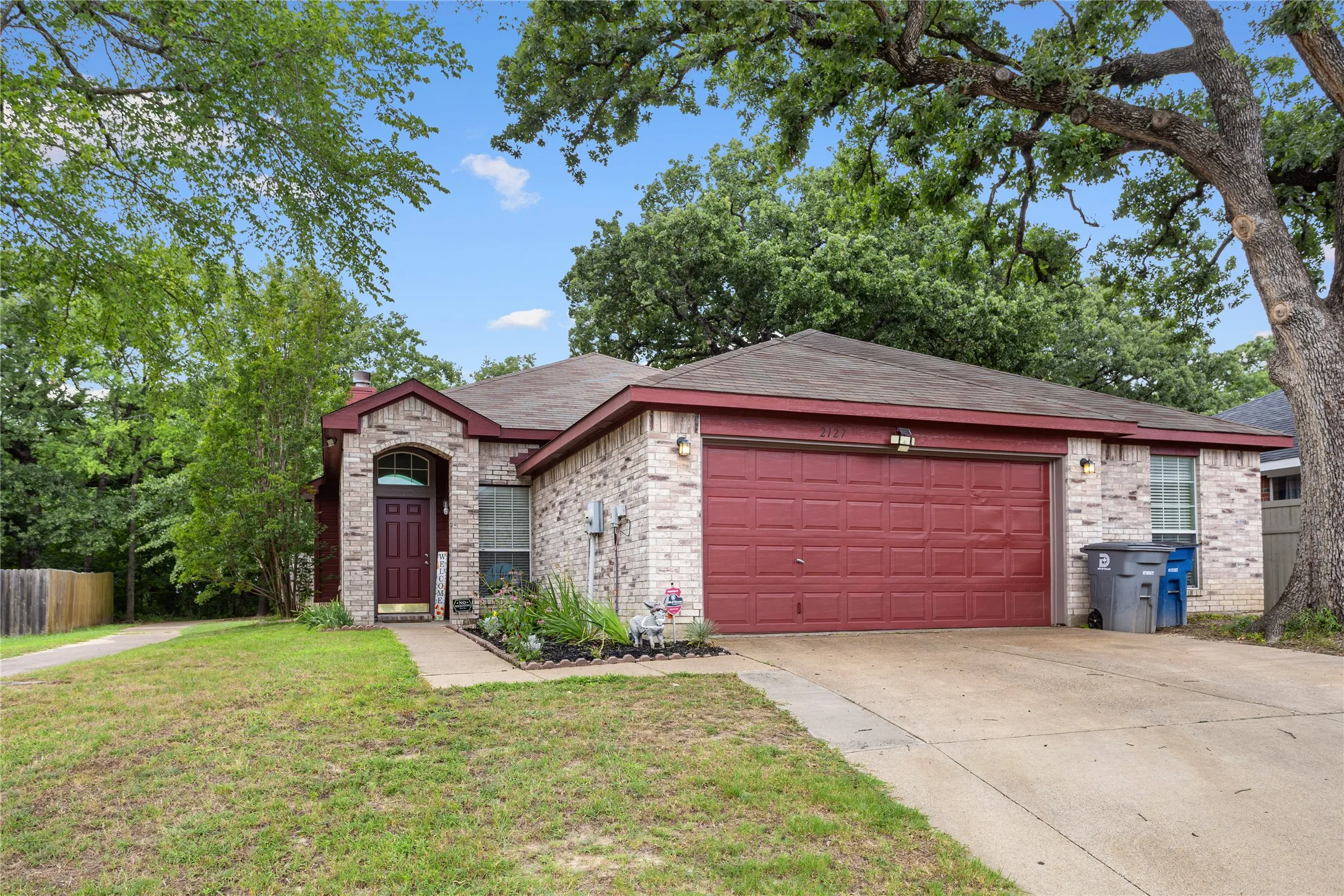 Brick facade with a red garage door and matching trim, featuring an arched entryway and a cultivated front garden bed