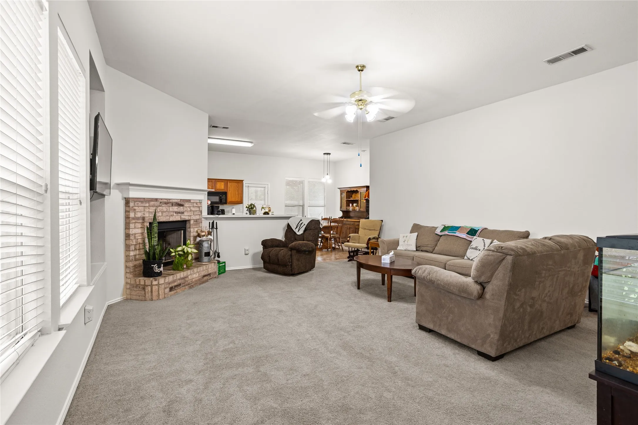 Living area featuring a brick fireplace, carpet flooring, and a ceiling fan