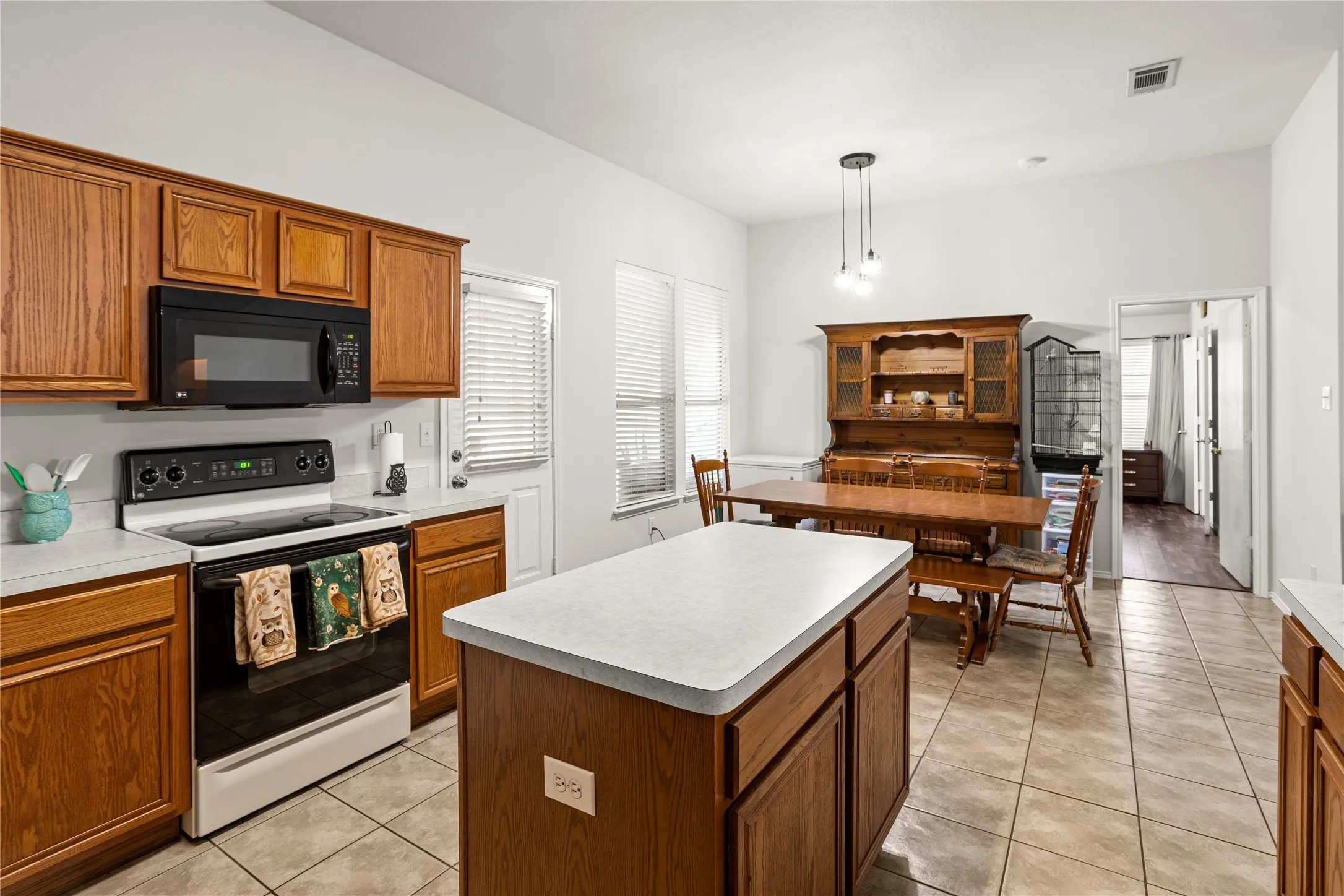 Kitchen featuring wood-finish cabinetry, a central island, a built-in microwave, an electric range, and tile flooring