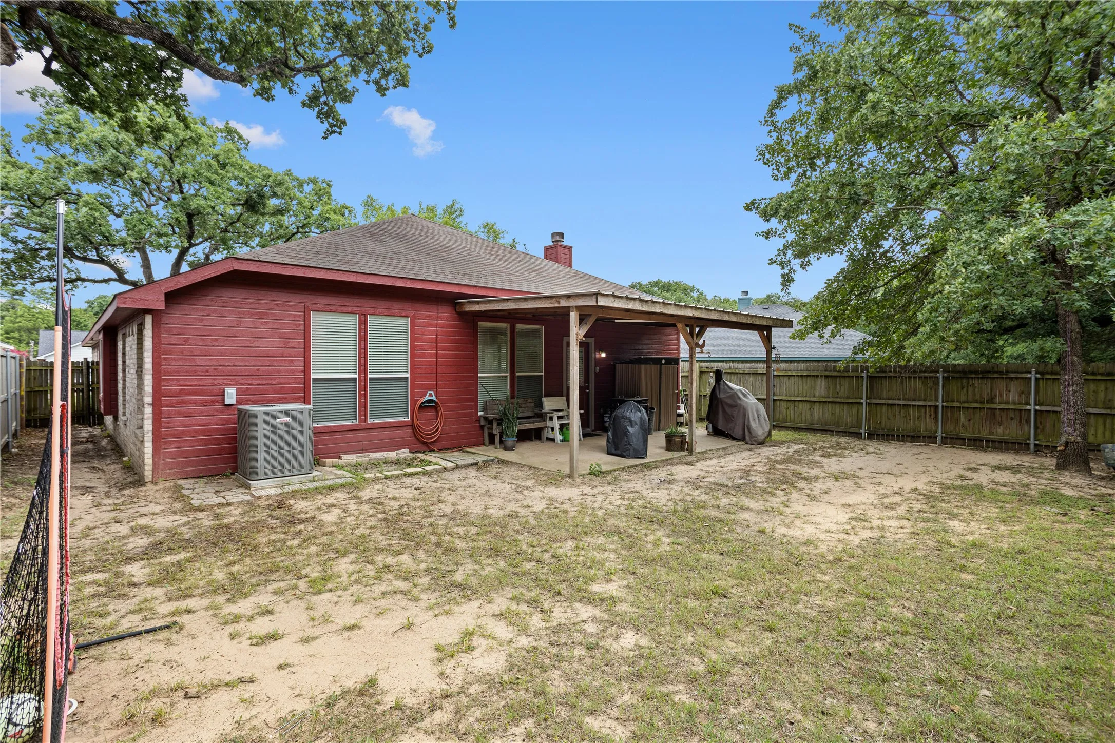 Expansive outdoor space featuring a covered patio, wood panel fencing, and mature trees
