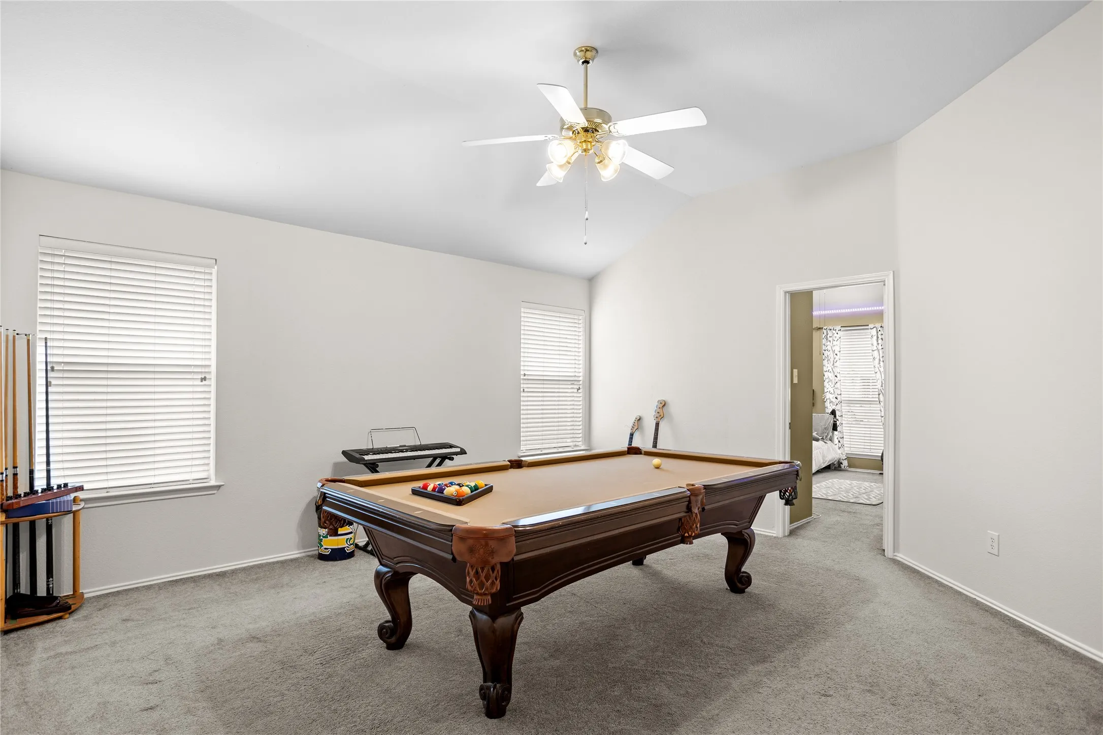 Vaulted ceiling with a ceiling fan, two windows with blinds, and light gray wall paint
