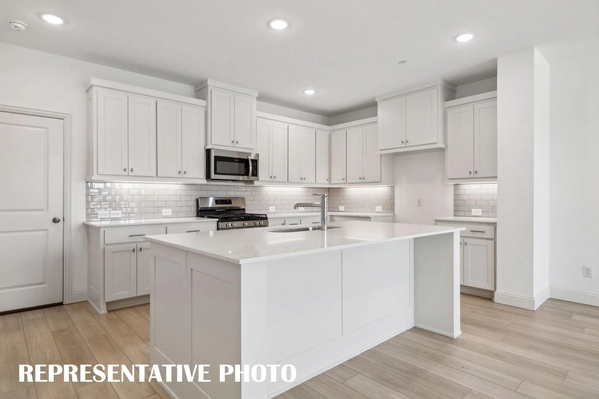 Kitchen featuring white shaker-style cabinetry, a central island with a solid surface countertop, stainless steel appliances, a tile backsplash, and wood-finish flooring