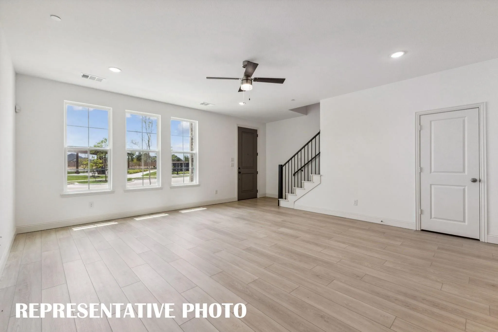 Spacious room featuring light wood-finish flooring, three large windows, a ceiling fan, and recessed lighting