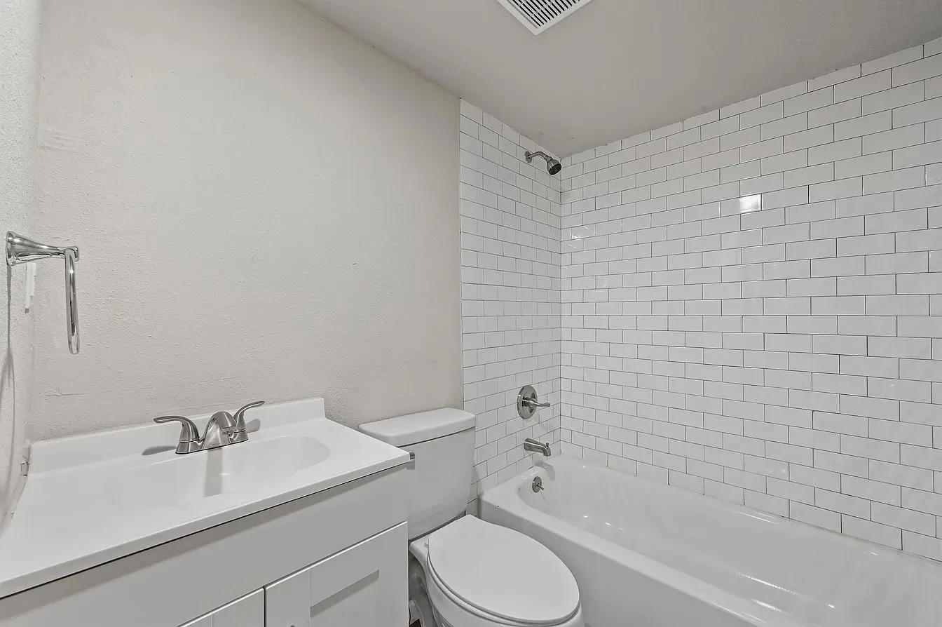 Bathroom featuring a white vanity with integrated sink, chrome faucet, toilet, and subway tile shower surround with a tub