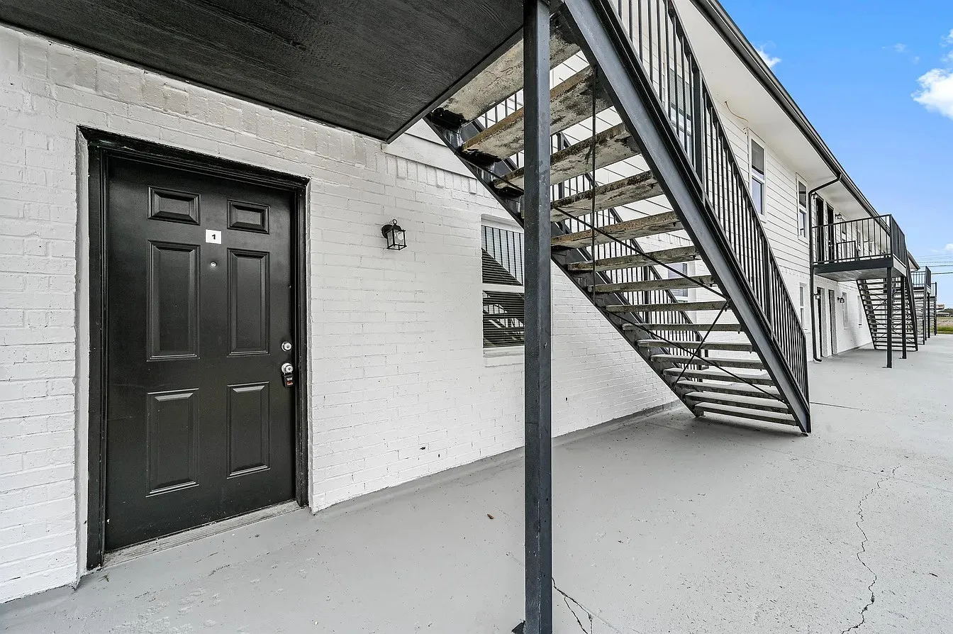 Black paneled entry door with exterior wall lantern and white painted brick facade