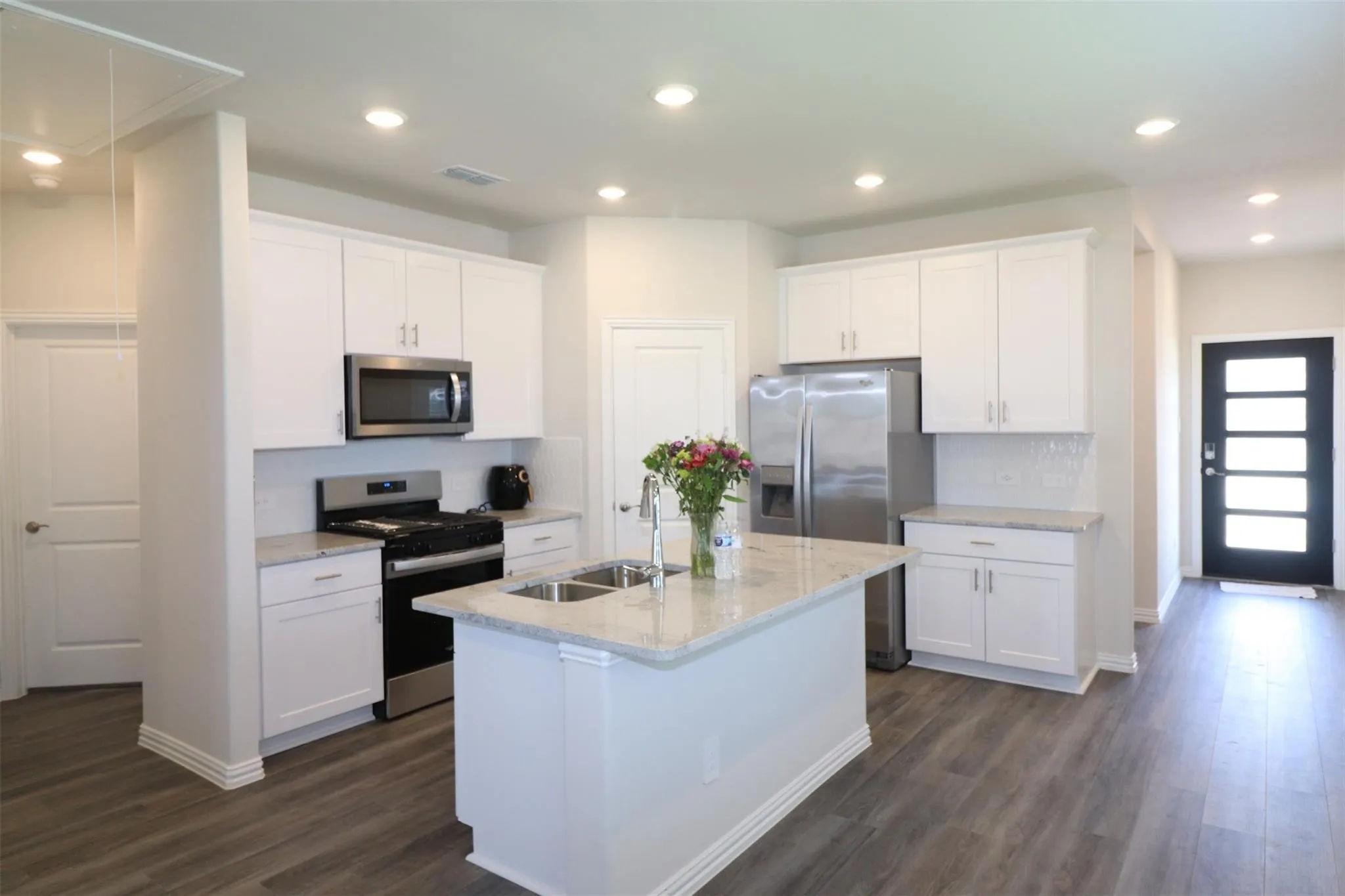 Kitchen featuring an island with dual sinks, white shaker-style cabinetry, stainless steel appliances, and grey wood-finish flooring