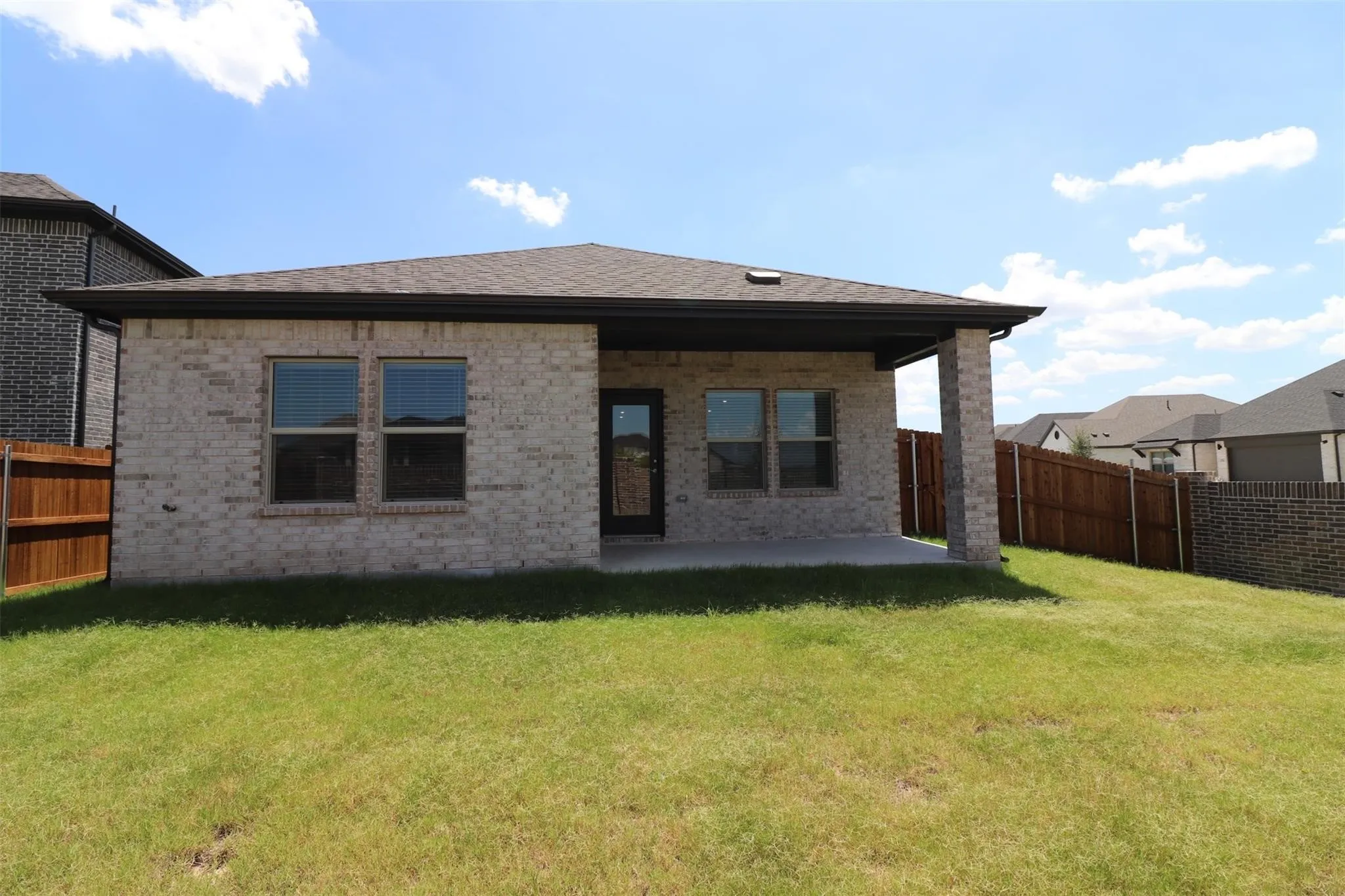 Rear exterior featuring light-colored brick, a covered concrete patio, a dark shingle roof, and a wood privacy fence