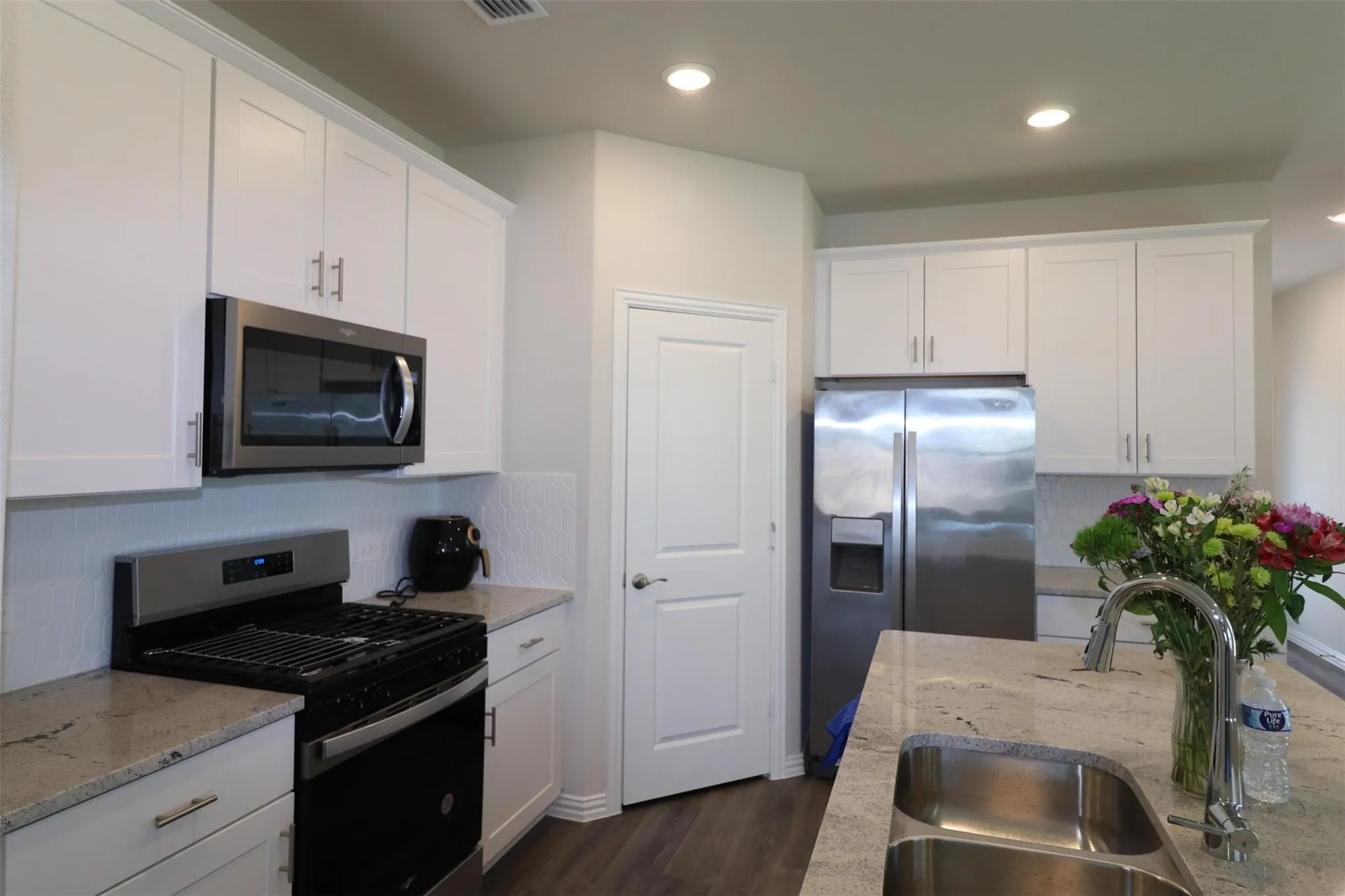 White shaker-style cabinetry with stainless steel hardware, stainless steel appliances, light-toned countertop, and recessed lighting