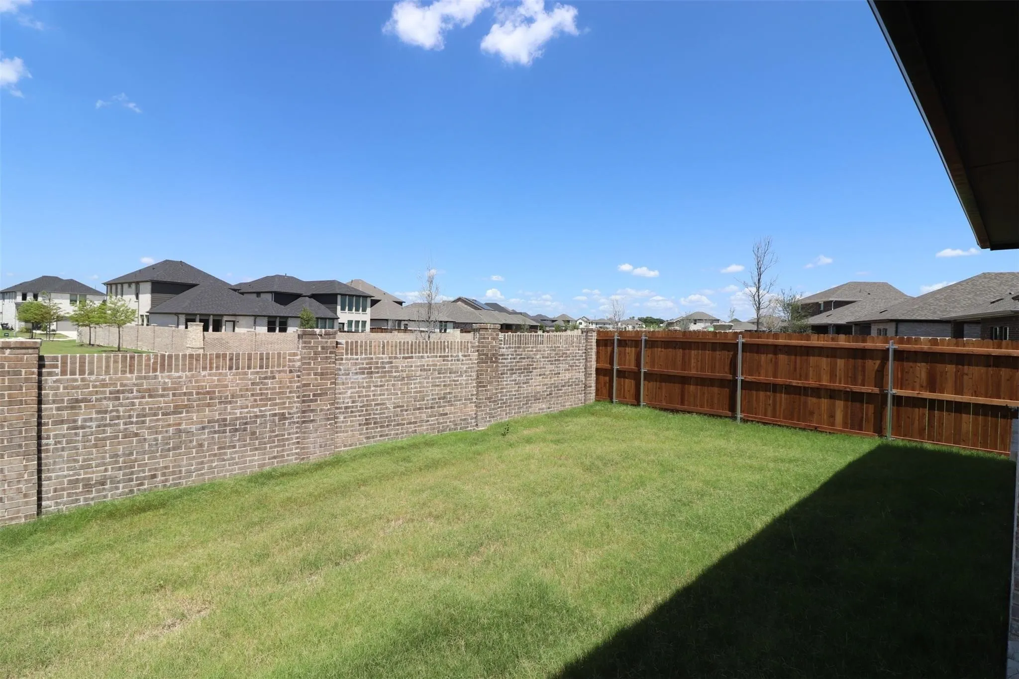 Expansive backyard featuring a manicured lawn, brick perimeter wall, and wood privacy fencing