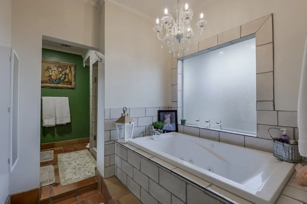 Spa-inspired primary bathroom featuring a freestanding soaking tub with subway tile surround, an oversized illuminated mirror with custom framing, polished chrome fixtures, and a crystal chandelier