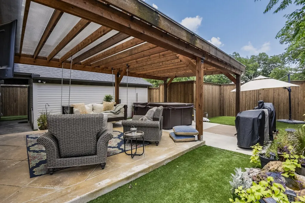 Expansive covered patio with exposed wood-beam ceiling and integrated lighting, featuring a concrete foundation and direct access to a manicured lawn