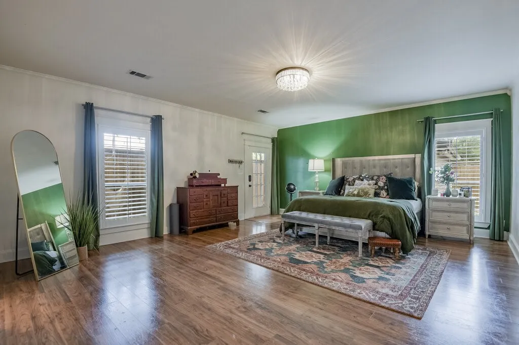 Spacious room featuring wood-finish flooring, a decorative ceiling light fixture, plantation shutters, and a paneled door