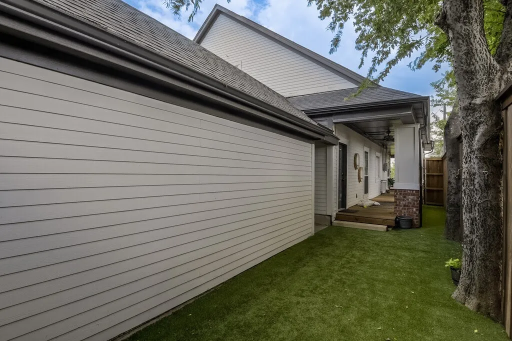 Modern home exterior showcasing horizontal fiber cement siding, a spacious attached garage with paneled door, covered entry porch, and a manicured lawn bordered by mature trees