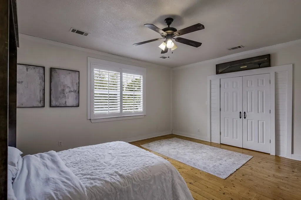 Spacious primary bedroom featuring hardwood flooring, a ceiling fan with integrated lighting, and dual closets with white paneled doors