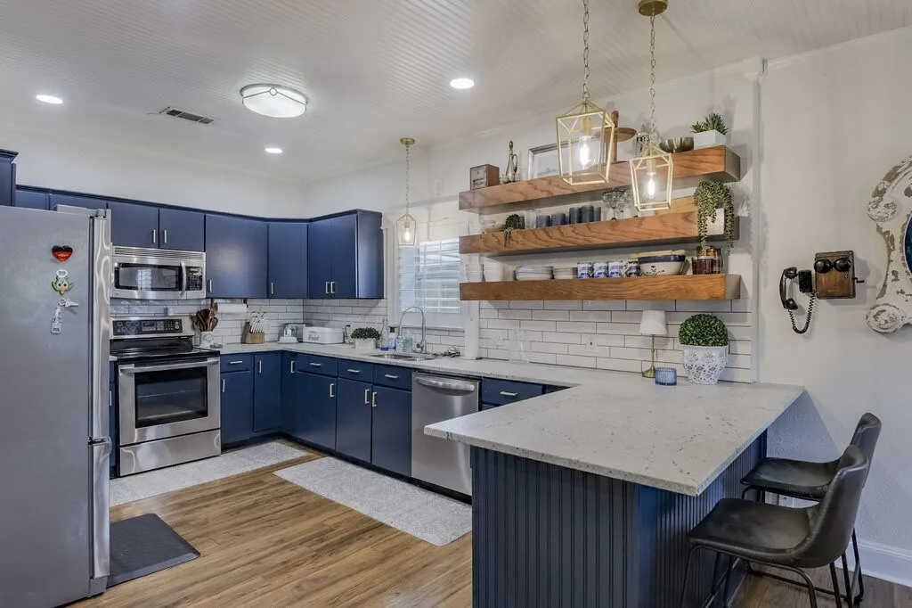 Kitchen featuring wood-finish flooring, dark blue cabinetry, stainless steel appliances, and open shelving