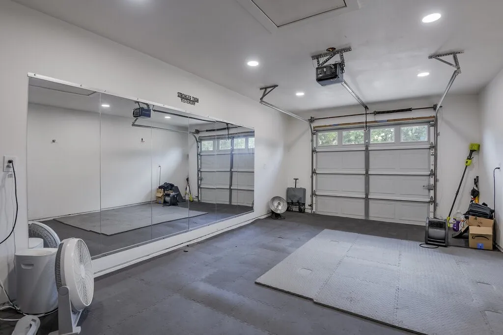 Dedicated garage space featuring a full-wall mirror, two overhead garage doors, recessed lighting, and textured floor mats
