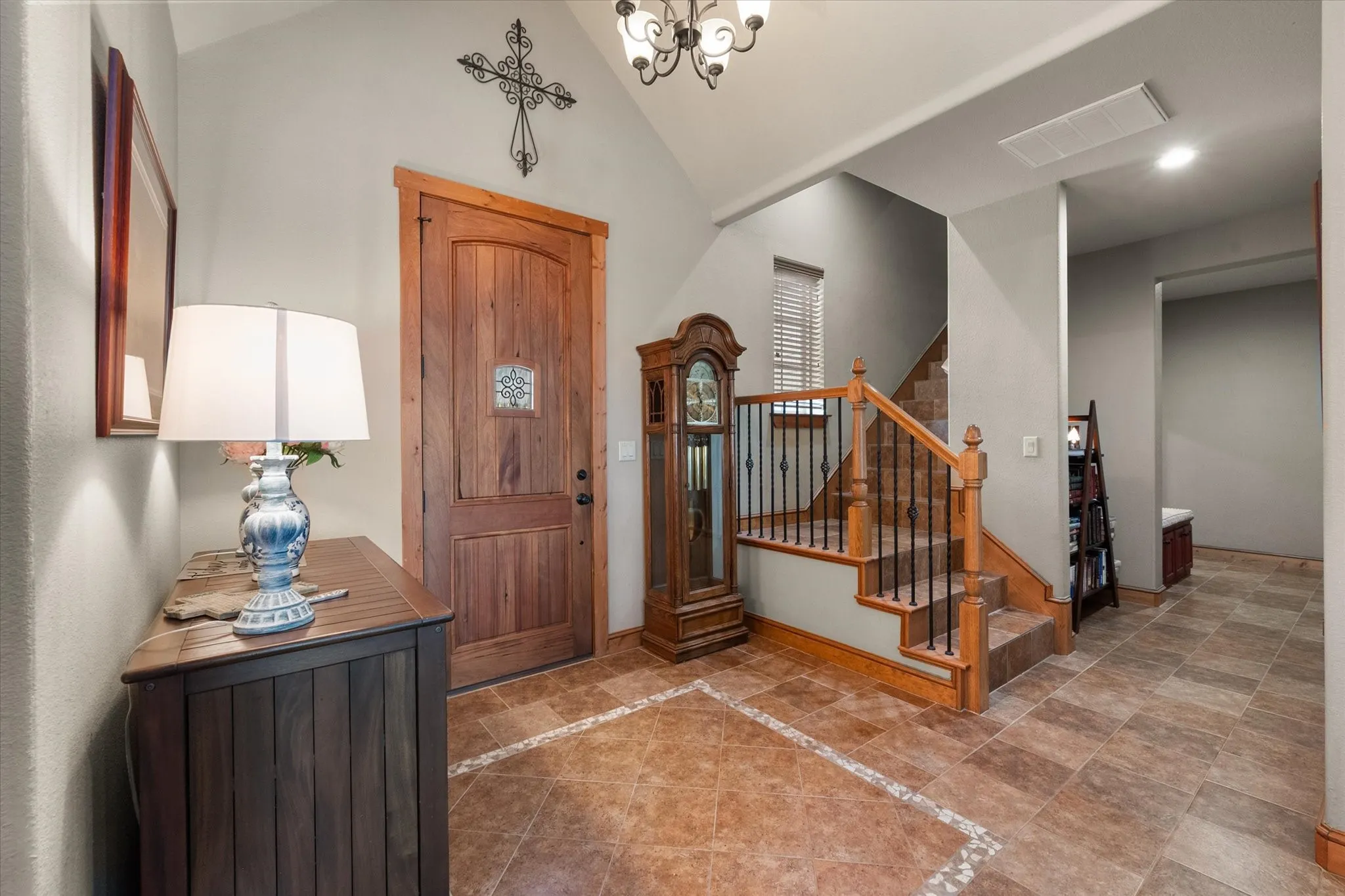 Warm and welcoming foyer features natural wood accents, tile flooring, decorative lighting, and staircase access to the bonus room.