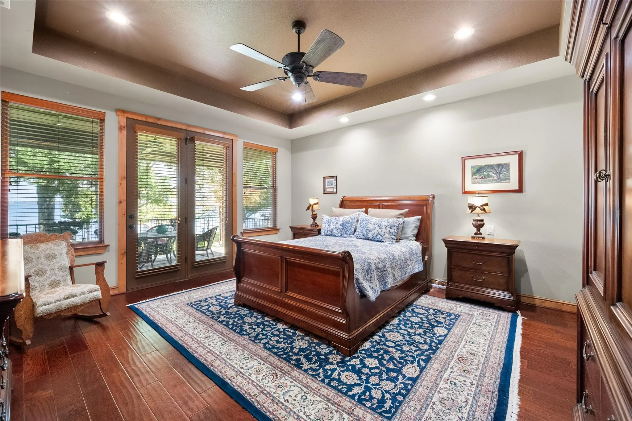 Spacious primary bedroom creates an inviting retreat with warm wood flooring, tray ceiling, abundant windows, and direct outdoor views.