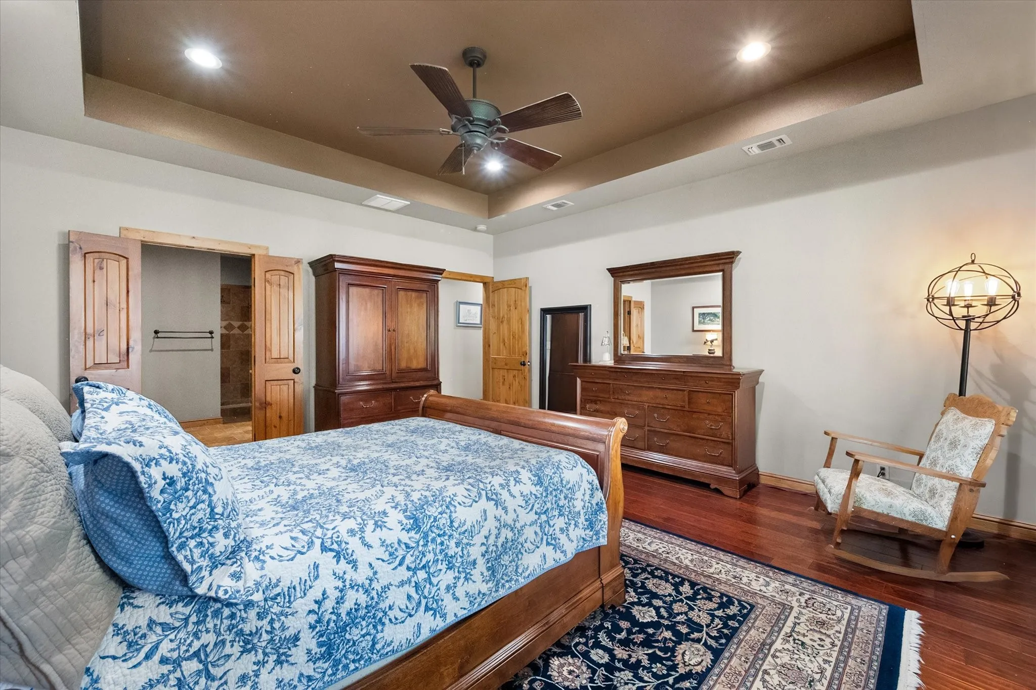 Generously proportioned primary suite combines rich wood flooring, a ceiling fan, multiple windows, and room for additional seating.