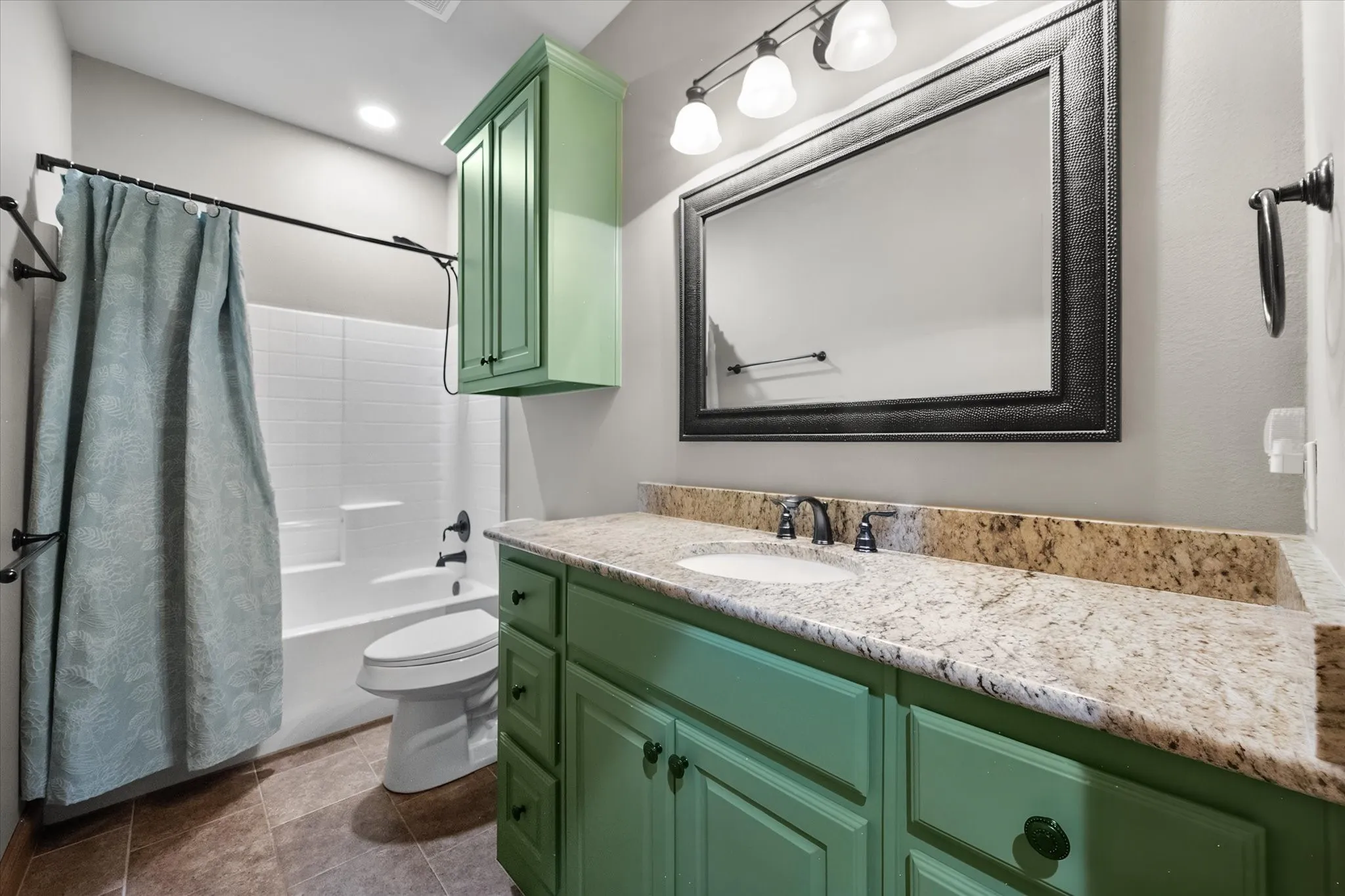 Full guest bathroom adds personality with a distinctive green vanity, granite countertop, tub and shower combination, and bright finishes.