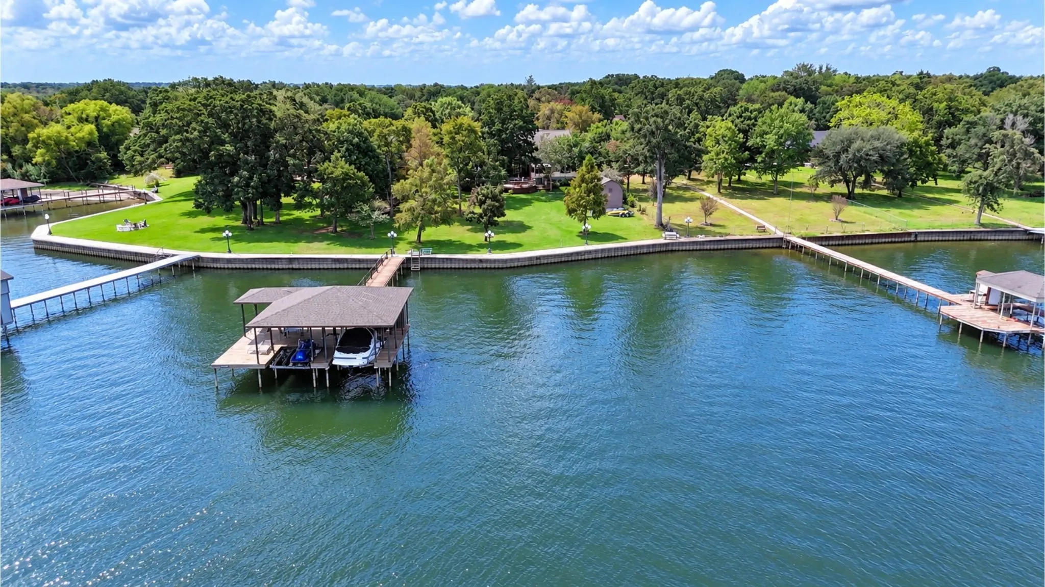 Aerial perspective highlights the home's waterfront setting, private boathouse, mature shoreline trees, and neighboring lakefront landscape.