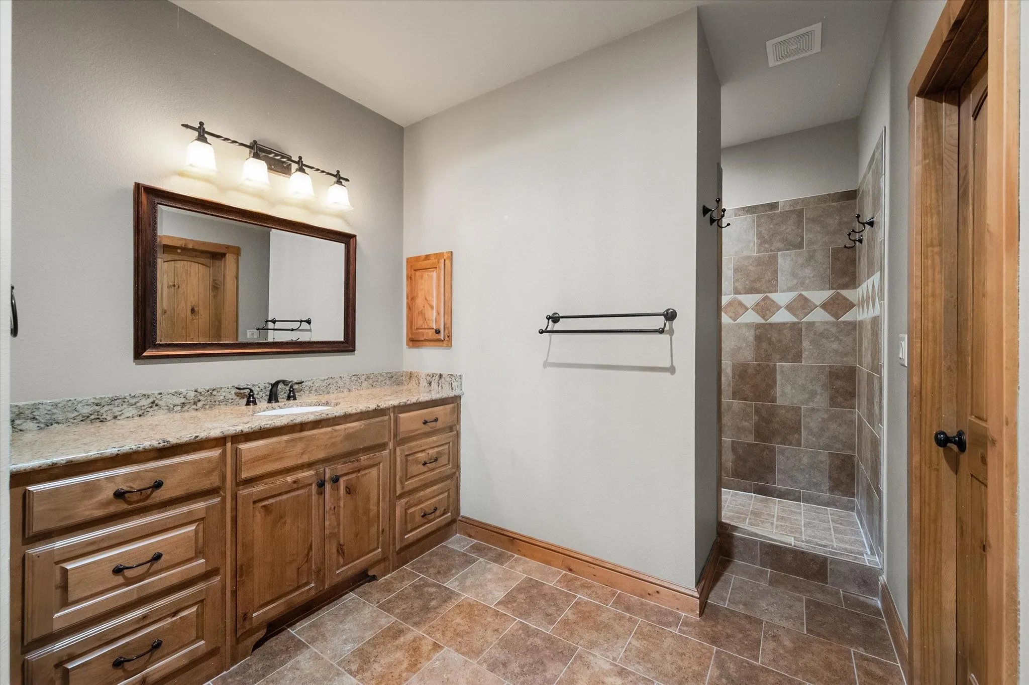 Well-appointed bathroom features a generous wood vanity, granite countertop, large mirror, and tiled walk-in shower.