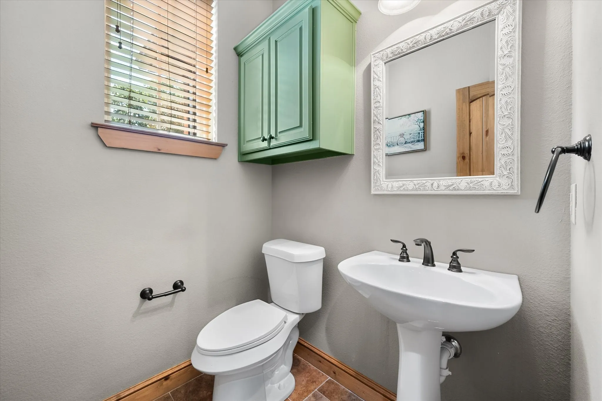Convenient half bath features a pedestal sink, natural light, and distinctive cabinetry that complements the home's warm character.