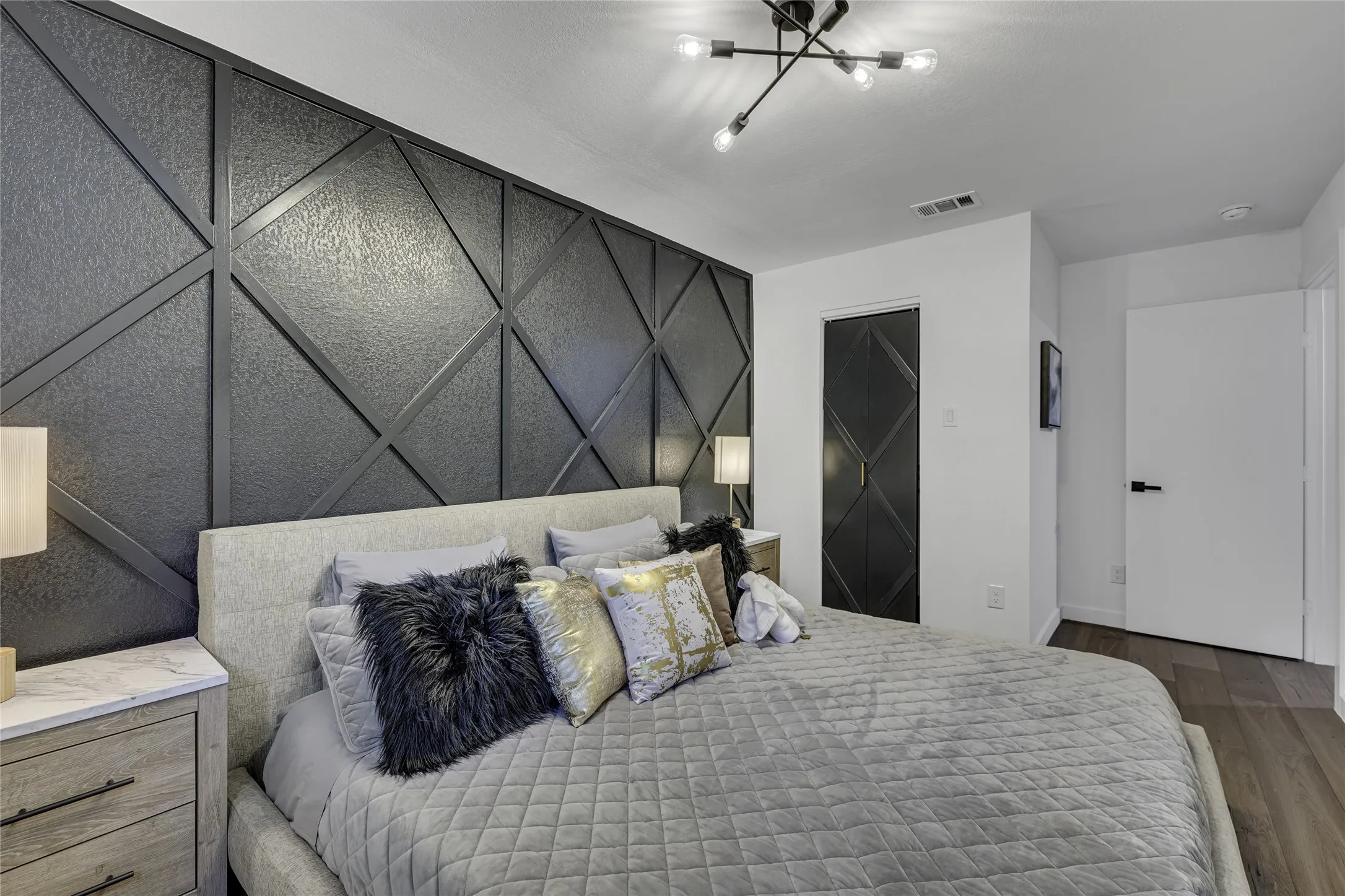 Bedroom featuring dark wood-type flooring, an accent wall, and a chandelier