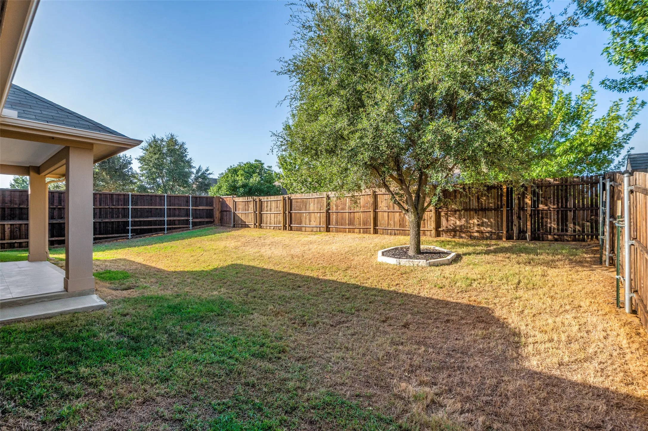Expansive backyard with a covered patio, privacy fencing, mature tree, and gate access
