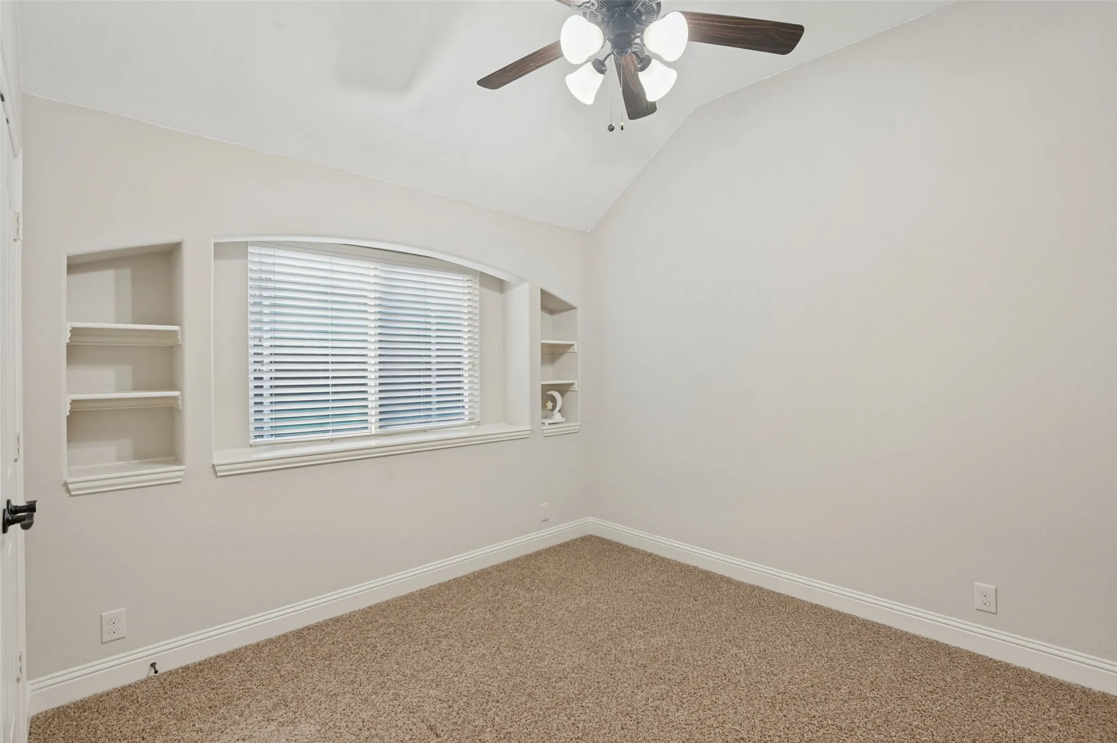 Vaulted ceiling, built-in shelving, arched window, ceiling fan with light fixture, and carpeted flooring