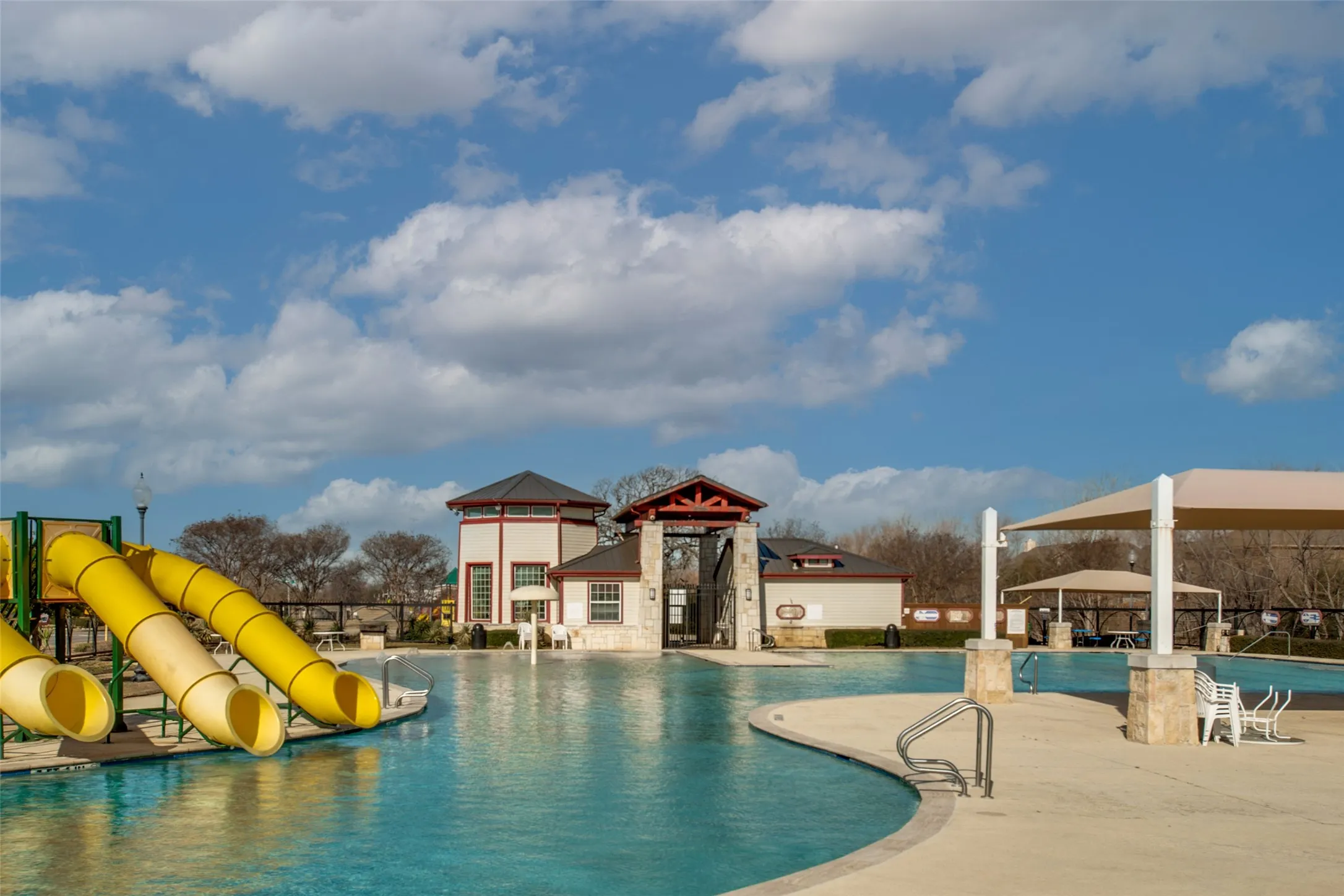 Swimming pool with curved edges, adjacent yellow waterslides, and a nearby building featuring a clock tower