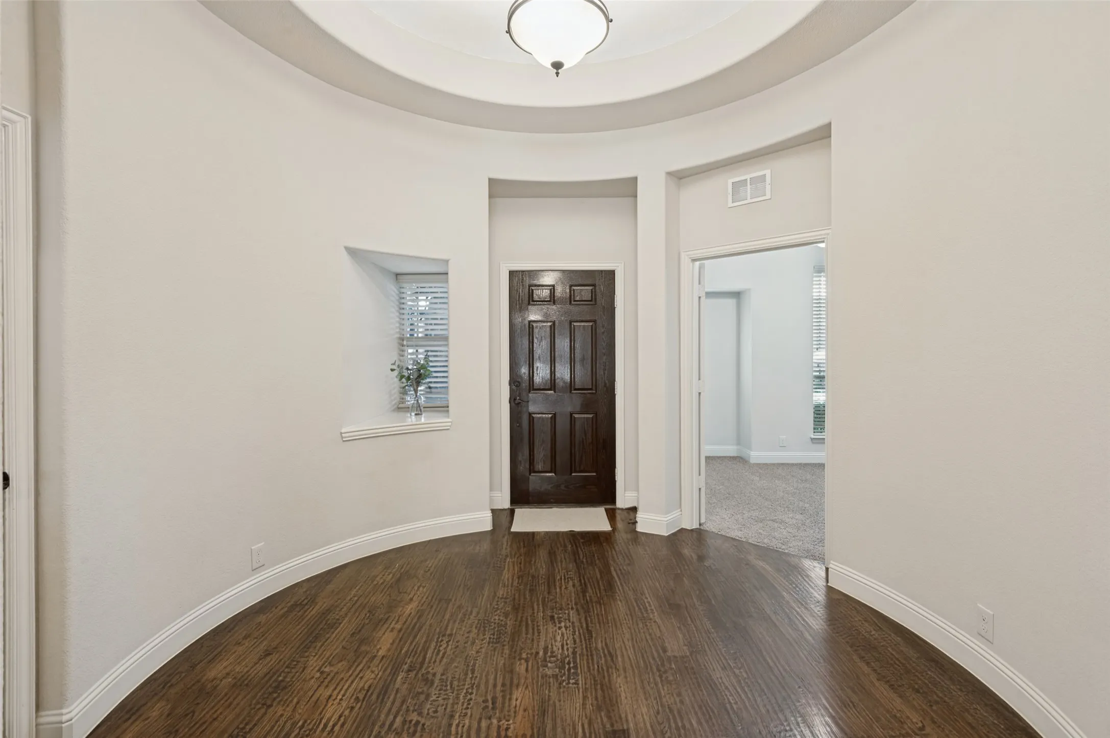 Curved entry hall with wood-finish flooring, a recessed window, and an overhead light fixture